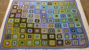 a granny square blanket in shades of blue and green