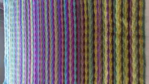 a wavy striped blanket in shades of blue, purple, and green