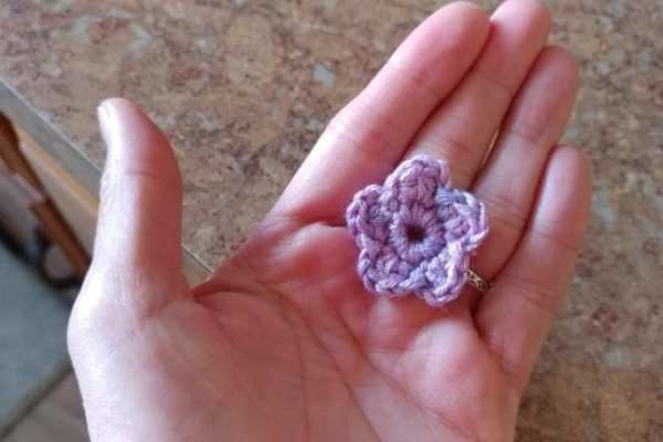 tiny crocheted flower resting in an open palm for scale