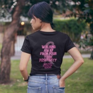 Back shot of a woman wearing a t-shirt that reads: Walking away from your toxic positivity. Breast cancer sucks.